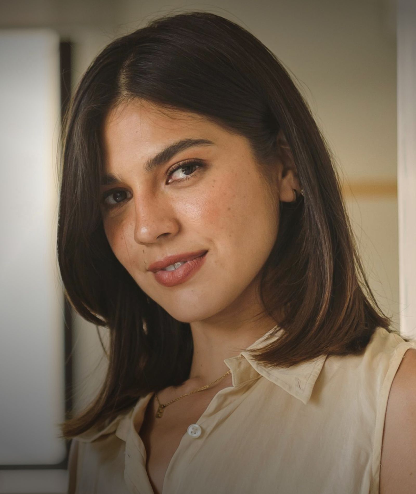 Woman smiling in a casual, light-colored blouse.